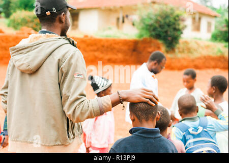 Bafoussam Kamerun - 06. August 2018: Junge afrikanische Lehrer streicheln Schule Junge beim Spielen im Freien Dorfschule lächelnd Stockfoto