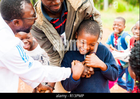 Bafoussam Kamerun - 06. August 2018: Die jungen afrikanischen Lehrern viel Spaß mit school Jungen beim Spielen ausserhalb des Dorfes Schule lächelnd Stockfoto