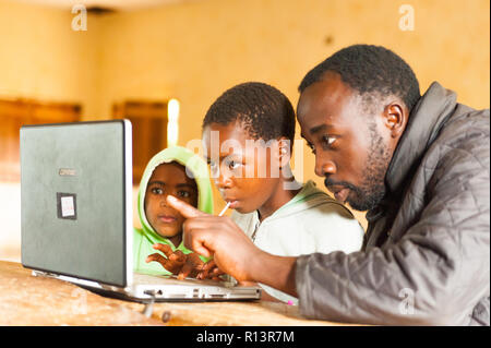 Bafoussam Kamerun - 06. August 2018: Junge afrikanische Lehrer die Kinder in der Schule lernen-Technologie mit dem Computer verbunden Stockfoto