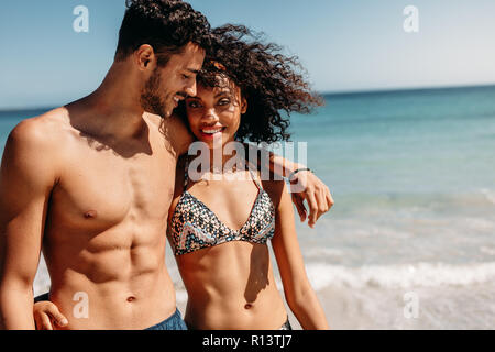 Romantisches Paar Walking am Strand zusammen an einem sonnigen Tag. Lächelnd Mann zu Fuß am Strand mit Freundin legte seinen Arm um ihre Schulter. Stockfoto