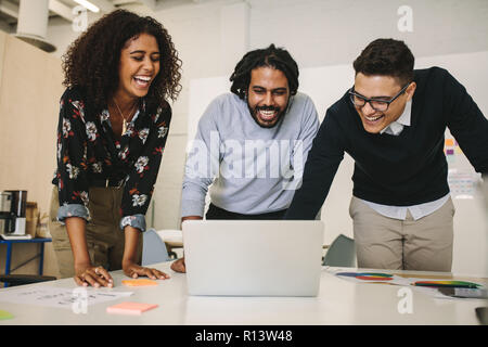 Geschäftsleute, die Spaß bei der Arbeit haben und lachen. Geschäftskollegen, die zusammen im Büro stehen und einen Laptop anschauen und lachen. Stockfoto