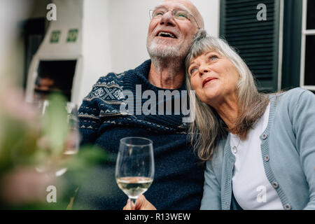 Ältere Frau ihren Kopf auf die Schulter ihres Mannes hält ein Glas Wein. Alte Paar sitzen entspannt zu Hause zusammen, Wein trinken. Stockfoto