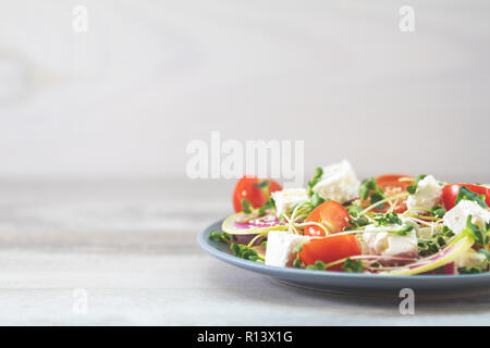 Gesund lecker lecker Salat mit Tomaten, Radieschen, Käse, Sprossen und Sesam in der Platte auf hellem Holztisch, flacher Tiefe des Feldes. Stockfoto