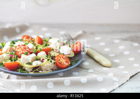 Gesund lecker lecker Salat mit Tomaten, Radieschen, Käse, Sprossen und Sesam in der Platte auf hellem Holztisch, flacher Tiefe des Feldes. Stockfoto