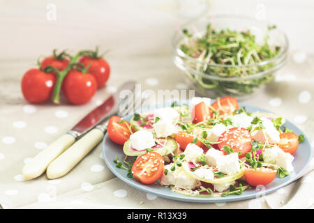 Gesund lecker lecker Salat mit Tomaten, Radieschen, Käse, Sprossen und Sesam in der Platte auf hellem Holztisch, flacher Tiefe des Feldes. Stockfoto