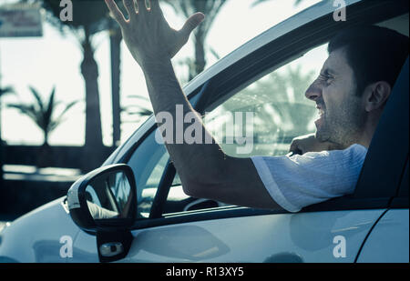 Aggressive Mann gestikuliert mit der Hand aus dem Fenster während der Fahrt. Verrückte Fahrer schreien aus dem Auto an einem sonnigen Tag. Stress, Traffic rush hour Konzepte Stockfoto