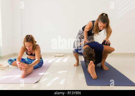 Weibliche Yoga Lehrer helfen jungen Mann in marichyasana darstellen. Yogi Schüler üben in helles Studio. Asana Anpassung, sitzend Haltungen Konzepte Stockfoto