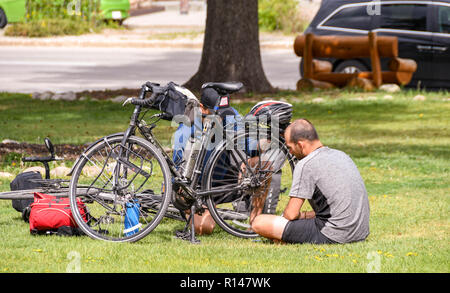 JASPER, AB, Kanada - Juni 2018: Zwei Radfahrer Kontrolle einer Ihrer Fahrräder in einem Park in Jasper, Alberta. Stockfoto