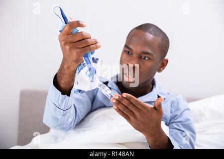 Nahaufnahme von einem besorgten jungen afrikanischen Mann suchen Bei CPAP-Maske Stockfoto