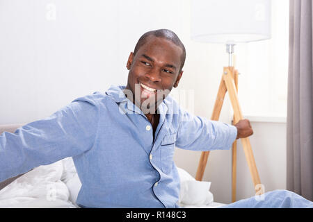 Portrait eines glücklichen jungen afrikanischen Mann sitzt auf dem Bett