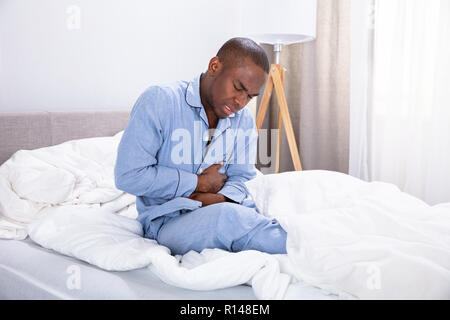 Afrikanischer Mann sitzen auf dem Bett Leiden, Bauchschmerzen Stockfoto