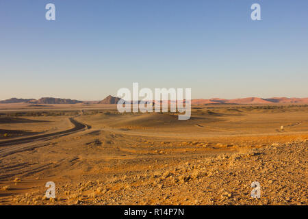 Querformat über dem Eingang zum Sossusvlei und Namib Naukluft National Park mit einem Heißluftballon Landung und einem geteerten Straße in den Dünen. Stockfoto