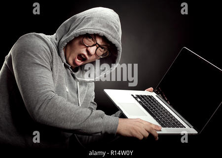 Ein Programmierer in der Haube und Gläser wütend Schreien und ist über einen Laptop an die Wand zu werfen Stockfoto