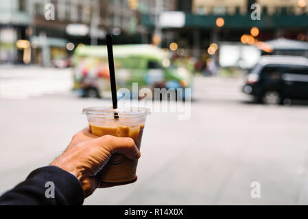 Männliche Hand eine Tasse iced gebrühten Kaffee trinken gegen das Stadtbild von New York City mit Platz für Kopie Stockfoto