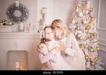 Schöne junge Mutter mit ihrer Tochter in das Innere des Neuen Jahres in der Nähe der Weihnachtsbaum. Das Konzept der Winterurlaub: Neues Jahr und Christma Stockfoto