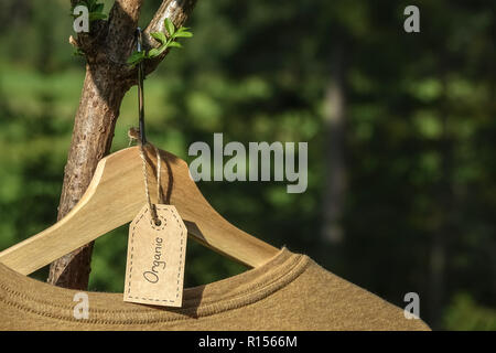 Organische Kleidung. Natürliche farbige T-Shirt hängen auf hölzernen Kleiderbügel in Elder berry Tree. Eco Textile Tag. Grüne wald, natur im Hintergrund. Stockfoto