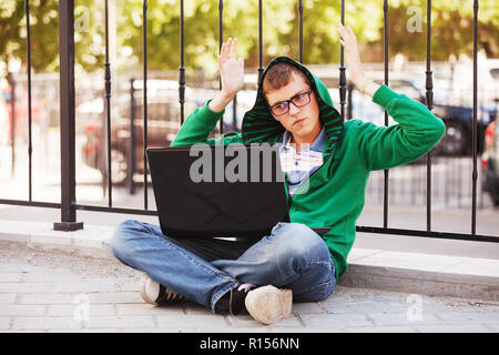 Junger Mann mit Laptop auf dem Bürgersteig in der Stadt. Stockfoto