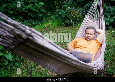 Mann in einer Hängematte im tropischen Dschungel Lügen und arbeitet auf einem Laptop. Brasilien Stockfoto