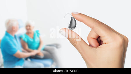 Arzt zeigt ein Hörgerät der letzten Generation mit unfokussierten älteren Patienten im Hintergrund Stockfoto