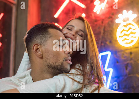 Happy gemischtrassiges Paar sitzt, die auf dem Hintergrund der Neonröhren. Stockfoto