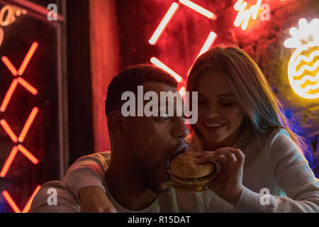 Junge Frau Feeds ein Mann einen Burger. Paar, Spaß zu haben. Stockfoto