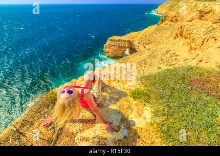 Blonde Frau genießt die natürliche Brücke in Kalbarri Nationalpark, Western Australia. Backpacker Mädchen über malerische Klippen der Küste des Indischen Ozeans. Australische Outback reisen. Blauer Himmel, Sommer sonnigen Tag Stockfoto