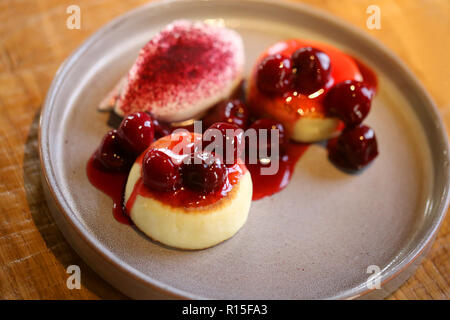 Makro Foto von leckeren hellen Käse Kuchen mit Kirsche Konfitüre und Sauerrahm auf einer Platte Stockfoto