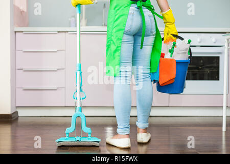 Frau mit Mop und Kunststoffeimer mit Bürsten, Handschuhe und Waschmittel in der Küche Stockfoto