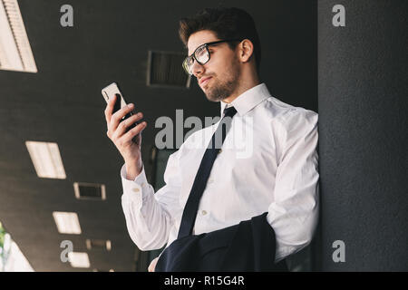 Bild von sachlich Mann in Anzug, außerhalb Gebäude aus Glas und mit Smartphone gekleidet Stockfoto