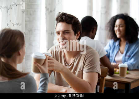 Vielfältigen, multi-ethnischen Paare sitzen an einem Tisch in Cafe trinken, heiße Getränke, Kaffee im Pappbecher gekoppelt, den Schwerpunkt auf die kaukasischen lächelnden Mann. Freunde sp Stockfoto
