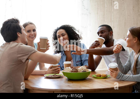 Diverse Freunde Mädchen und Jungs sitzen um den Tisch chatten Spaß trinken Kaffee im Pappbecher genießen die Zeit zusammen. Die Freundschaft zwischen den verschiedenen r Stockfoto