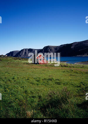 Norwegen, Finnmark, Nordkinnhalvoya, Rot lackiert Sommer Bauernhaus mit weiß lackierten Traufen und Fensterrahmen neben Sandfjorden in Bereich in tiefem Schnee im Winter abgedeckt. Stockfoto