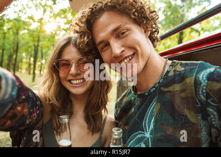 Foto der Schönen hippie Paar Mann und Frau lächelnd und unter selfie im Wald in der Nähe von Retro minivan Stockfoto