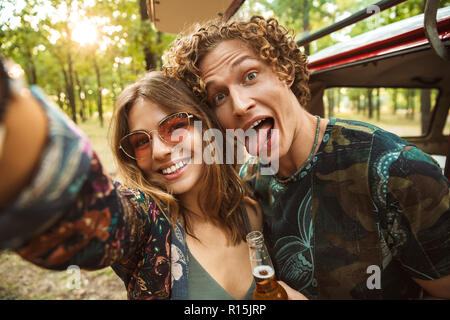 Foto des hübschen hippie Paar Mann und Frau lächelnd und unter selfie im Wald in der Nähe von Retro minivan Stockfoto