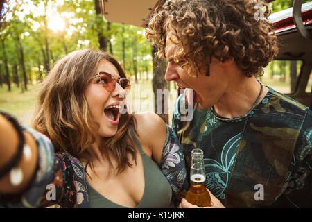 Foto von fröhlichen hippy Paar Mann und Frau lächelnd und unter selfie im Wald in der Nähe von Retro minivan Stockfoto