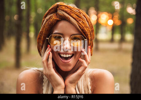 Foto von fröhlichen hippie Frau mit stilvollen Accessoires, Lächeln beim Laufen im Wald Stockfoto