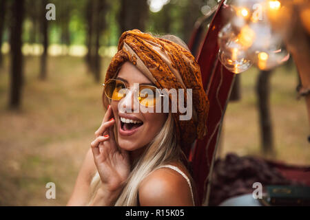 Foto des Blonden hippie Frau mit stilvollen Accessoires, lächelnd, während in Forest Camp ruhen Stockfoto