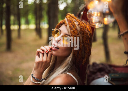 Foto der netten Nomadin tragen stilvolle Accessoires lächelnd während in Forest Camp ruhen Stockfoto