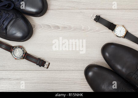 Zwei Paare von schwarzem Leder Herrenschuhe und zwei Armbanduhren auf grau Holz- Hintergrund. Herren Accessoires. Ansicht von oben Stockfoto