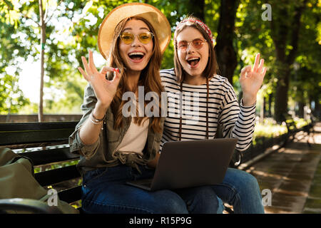 Foto der jungen emotional aufgeregt happy Damen Freunden draußen sitzen mit Laptop Computer Übersicht okay Geste. Stockfoto