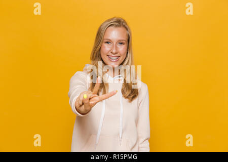 Foto von teenage Mädchen 16-18 mit Zahnspangen, Daumen hoch, über Gelb Hintergrund isoliert Stockfoto