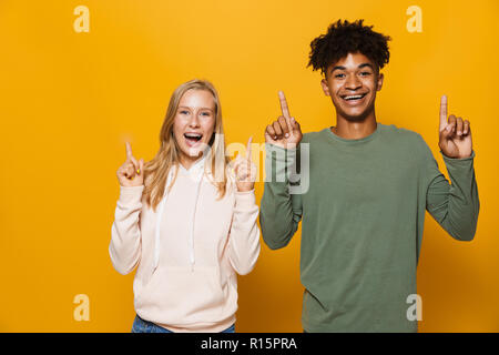 Foto von Multiethnischen Freunde Mann und Frau 16-18 mit Zahnspangen lachen und zeigen nach oben Copyspace über Gelb Hintergrund isoliert Stockfoto