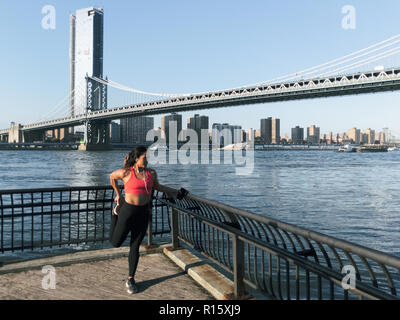 Junge athletische Frau erstreckt sich entlang des Wassers in New York City Stockfoto