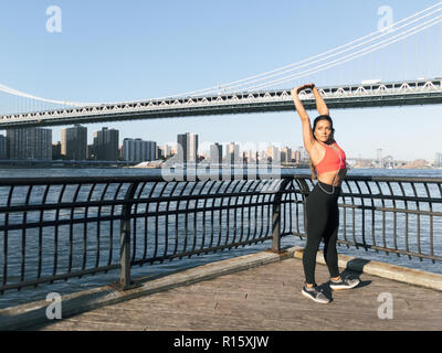 Junge athletische Frau erstreckt sich entlang des Wassers in New York City Stockfoto