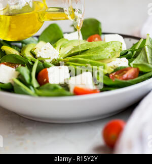 Gesunde Salate. Gießen Olivenöl über den Salat mit Avocado, Fetakäse, Spinat, Tomaten Stockfoto
