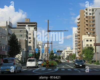 Blick auf eine breite Hauptstraße in der Stadt von Okayama, mit hohen Gebäuden, Autos und Fahrbahnmarkierungen; Western Honshu, Japan Stockfoto