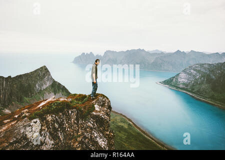 Man Reisende allein stehend auf Cliff mountain Kante über dem Fjord Meer Abenteuer Lifestyle Urlaub im Freien in Norwegen Einsamkeit Gefühle Stockfoto