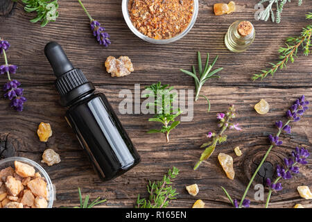 Flaschen des wesentlichen Öls mit Weihrauch, tulsi, herzhaften und anderen Kräutern auf einem hölzernen Hintergrund Stockfoto