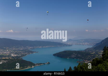 Drei Gleitschirme fliegen hoch über dem See von Annecy Frankreich Stockfoto