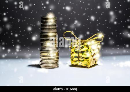 Das neue Jahr still-Leben mit einem Stapel von Goldmünzen und eine Box mit einem Geschenk auf einem dunklen Hintergrund mit fallendem Schnee Stockfoto